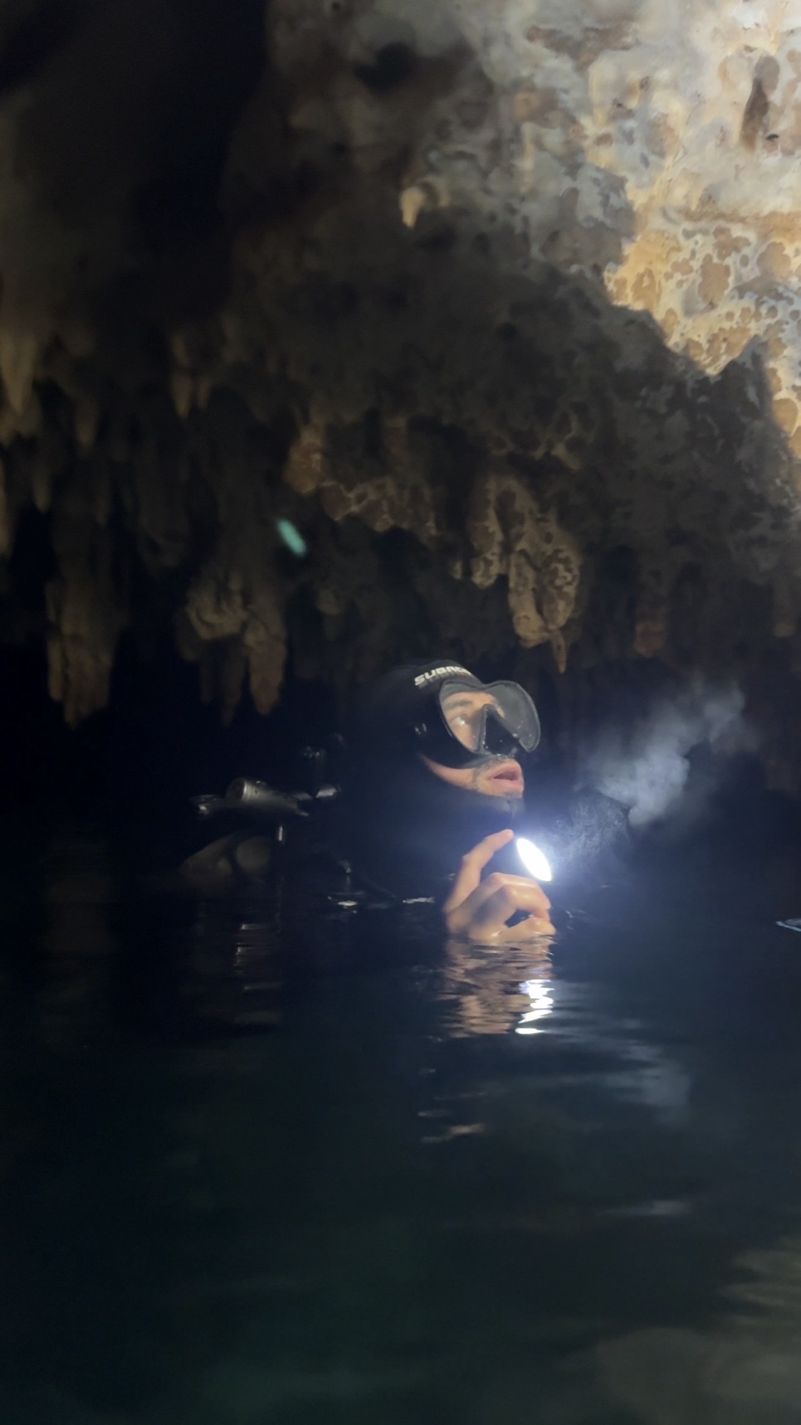 Diver surfaced inside a cave, lit by torchlight